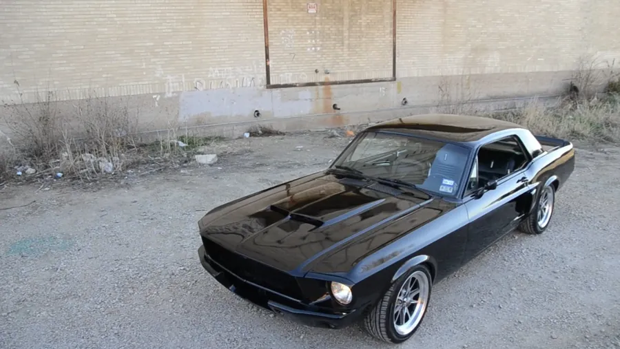 Black 1967 Mustang coupe with a vinyl top, parked on gravel.