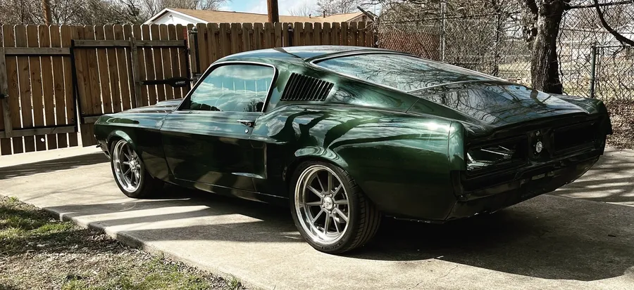 Dark green 1967 Mustang fastback on a driveway, rear three-quarter view.