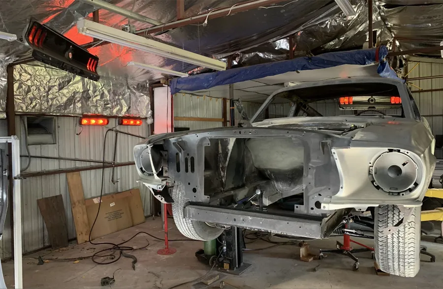 Bare Mustang shell on a rotisserie inside a foil-lined paint booth.