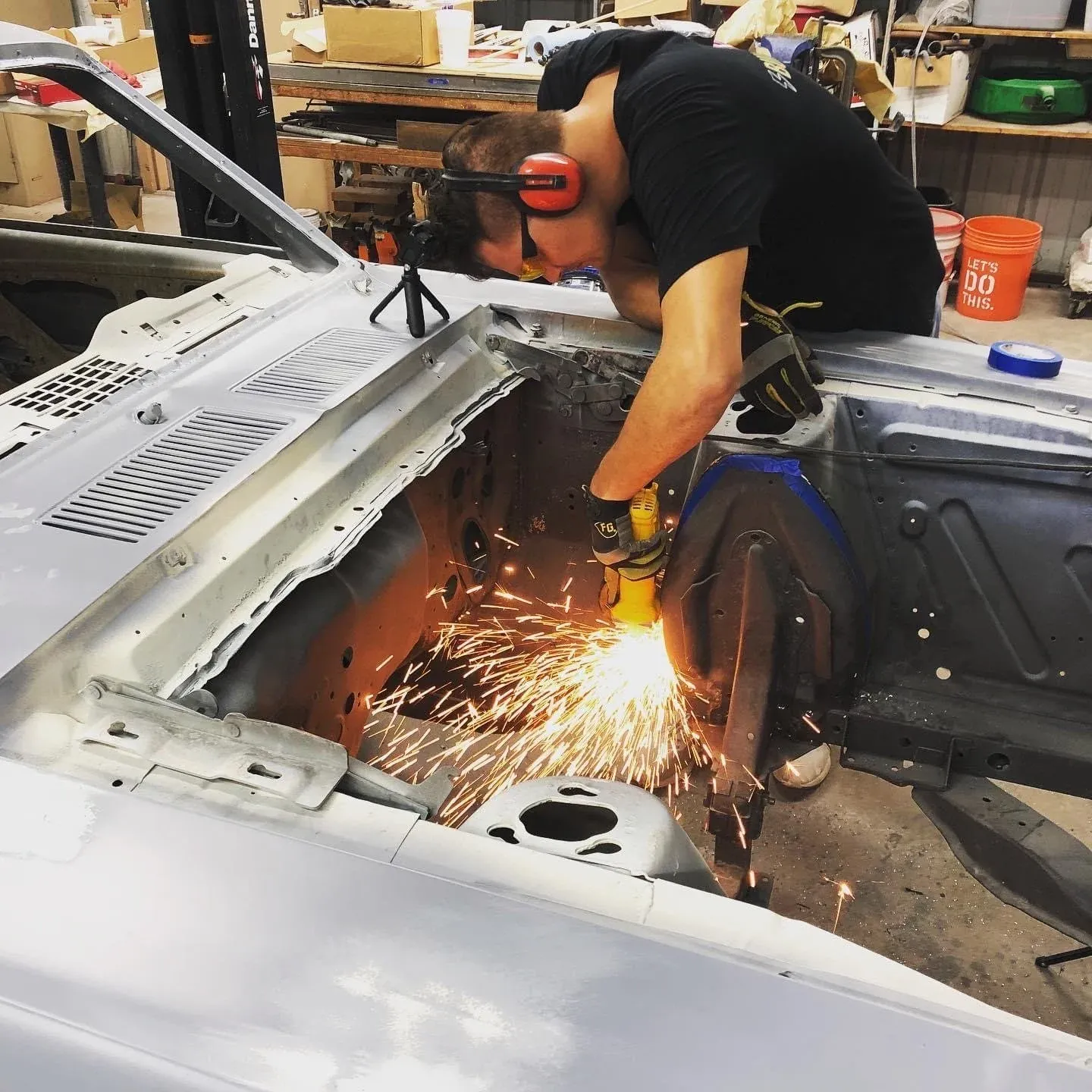 Brian grinding a seam on a classic Mustang body, sparks flying in the engine bay.